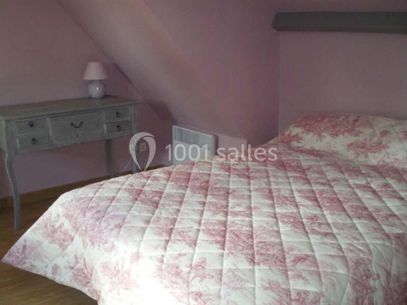 Chambre avec un lit double couvert d'une couette rose à motifs, une table grise et une lampe sur un mur rose.
