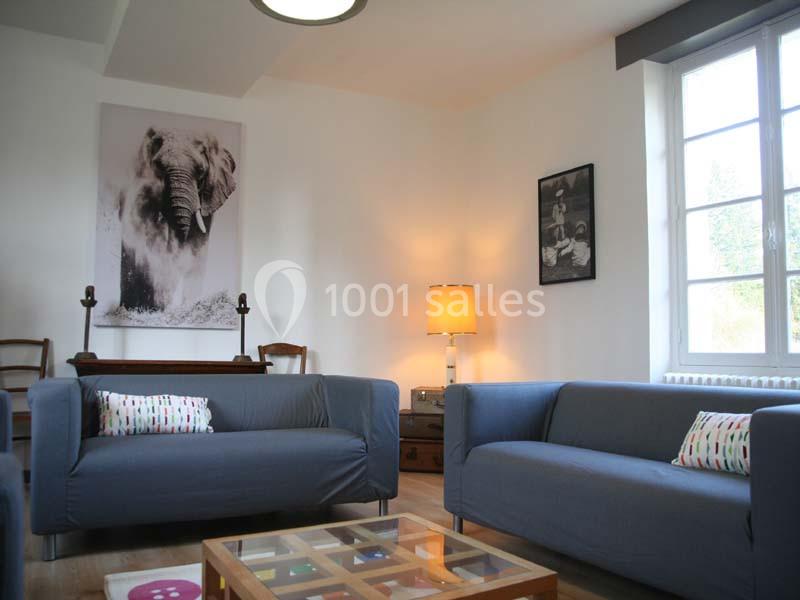 Deux canapés gris dans un salon lumineux avec une grande fenêtre, une lampe allumée et des décorations murales.