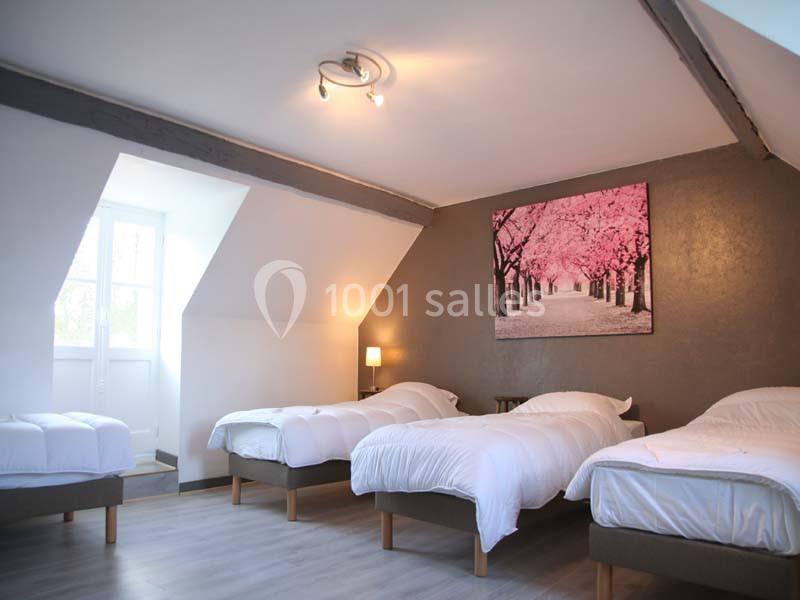 Chambre mansardée lumineuse avec trois lits simples, parquet clair, tableau mural et éclairage moderne.