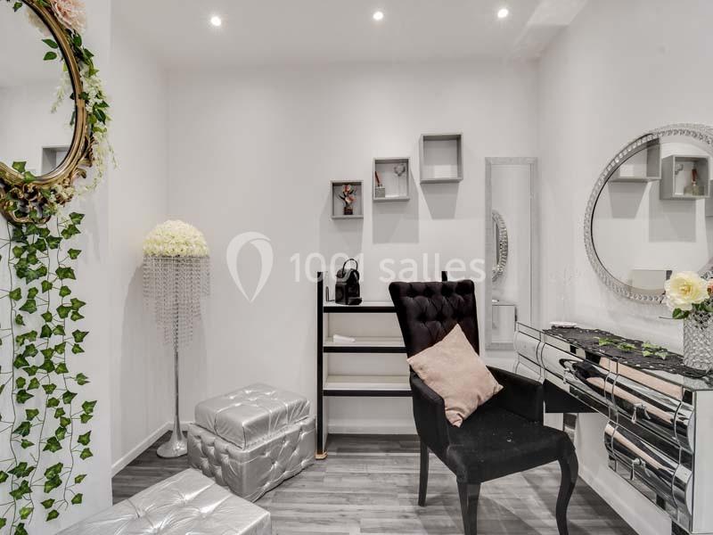 Salle lumineuse avec chaise noire, coiffeuse miroir, décorations florales et étagères murales dans un style élégant.