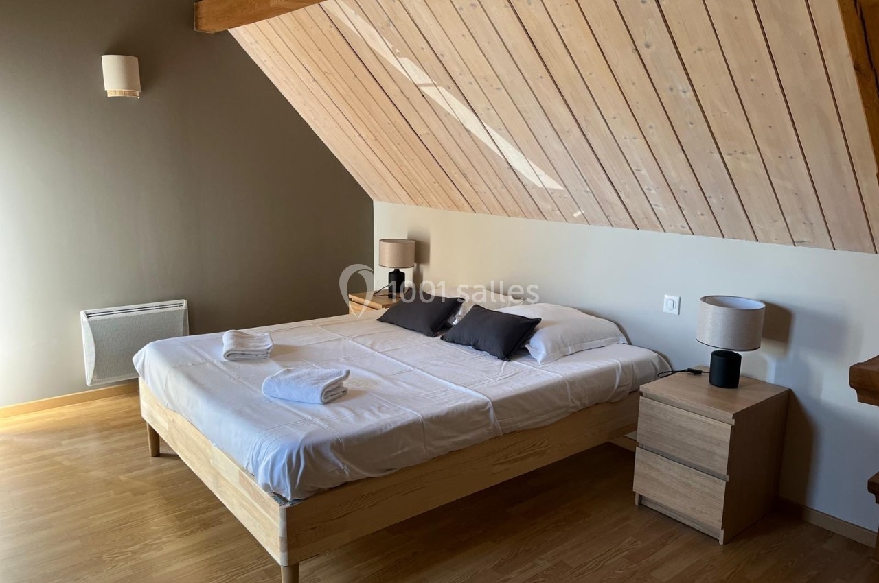 Chambre mansardée avec lit double, draps blancs, deux tables de chevet avec lampes et parquet en bois clair.