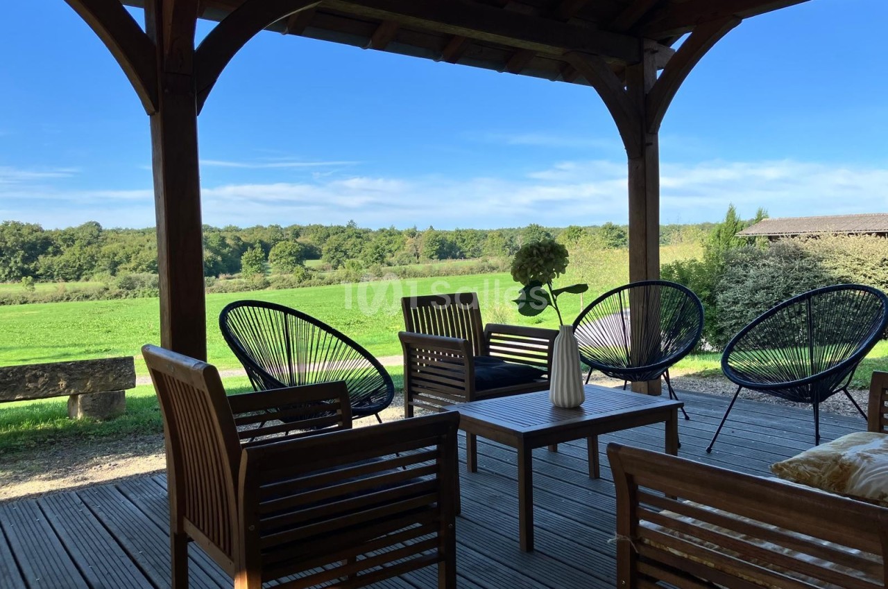Terrasse en bois avec mobilier de jardin, offrant une vue dégagée sur un paysage verdoyant et boisé.