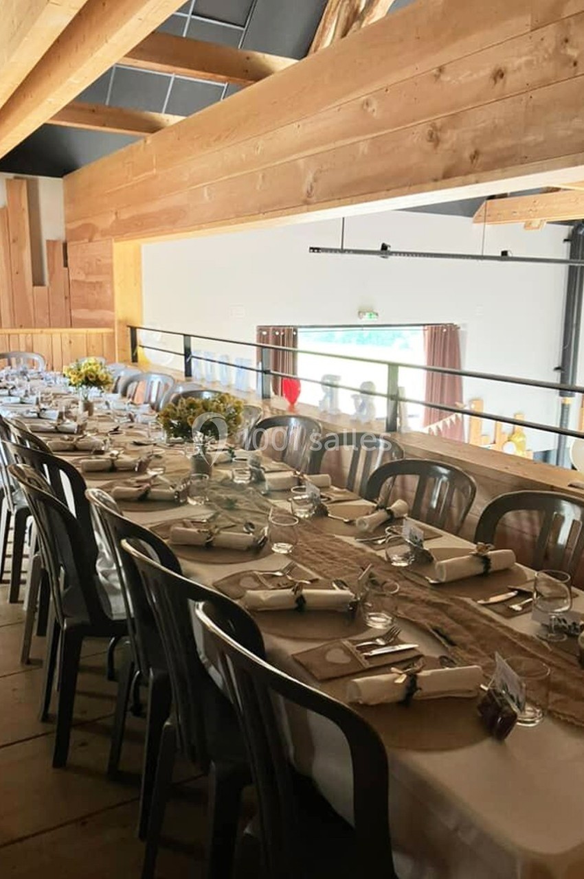 Table dressée avec nappes en lin, vaisselle et bouquets de fleurs jaunes, dans une salle en bois avec poutres apparentes.