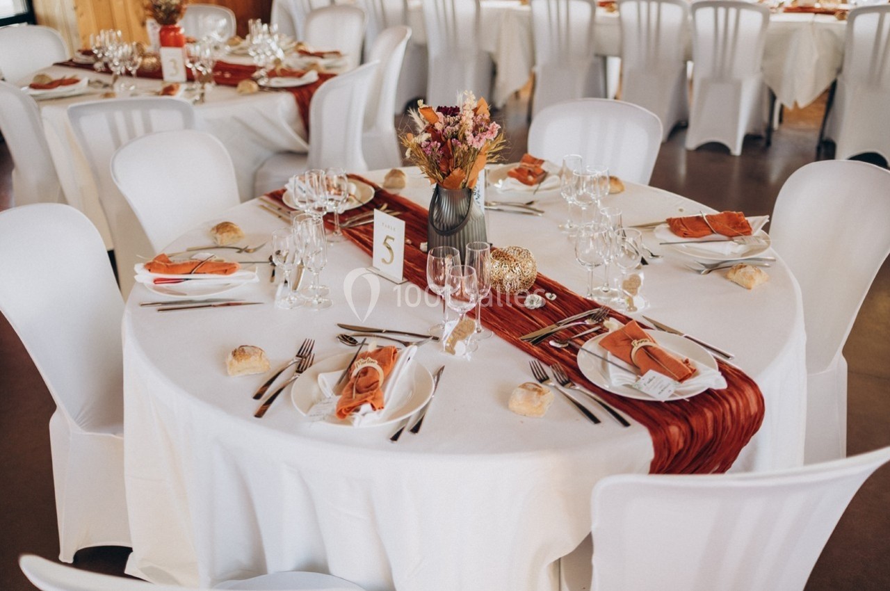 Tables rondes décorées pour un événement, avec nappes blanches, chemins de table rouges et bouquets de fleurs.