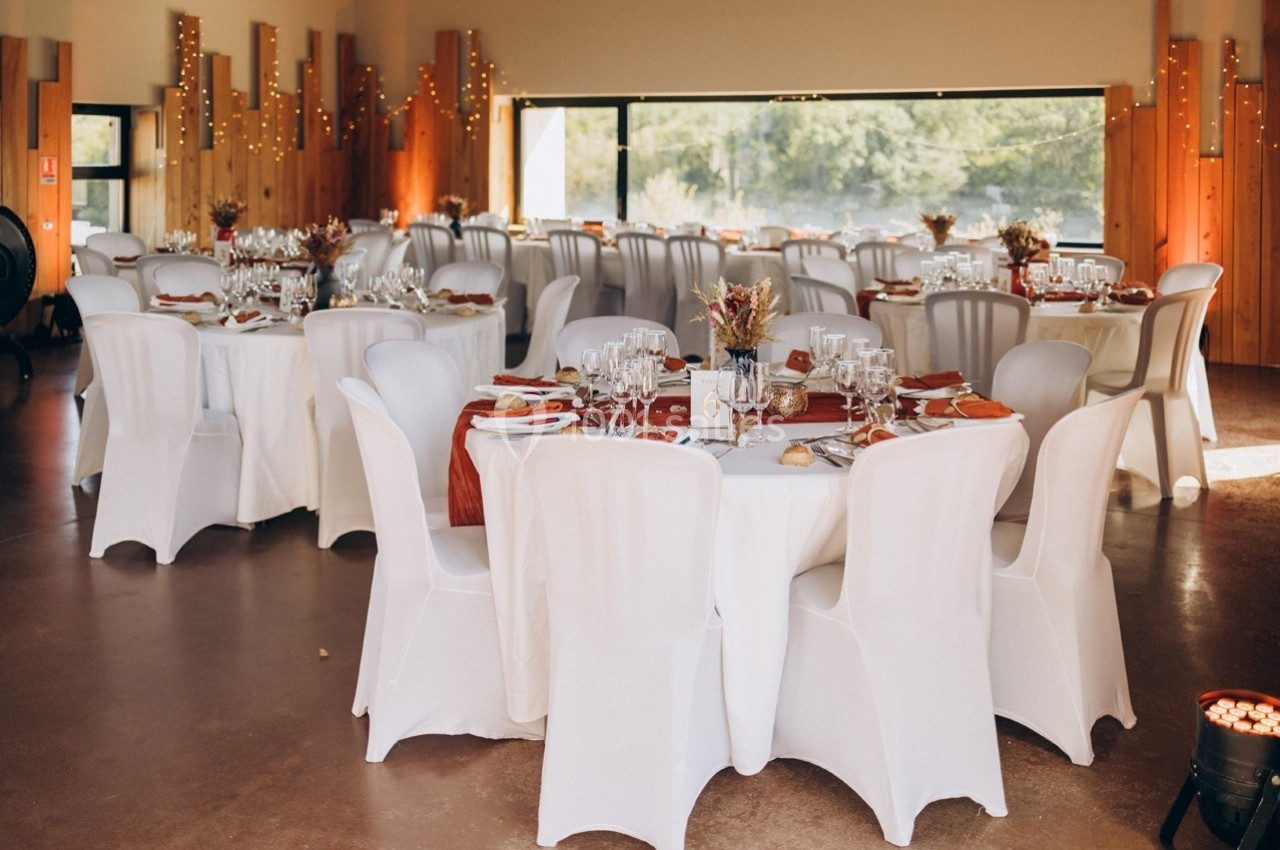 Salle de réception décorée avec des tables rondes dressées, nappes blanches et ornements automnaux.