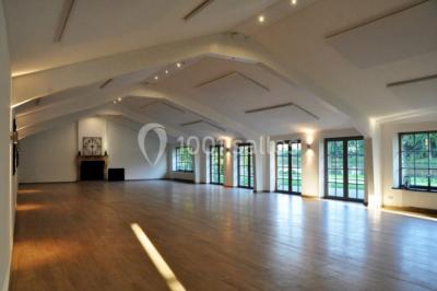 Salle de réunion lumineuse sous combles avec poutres apparentes, tables, chaises et écran de projection installé.