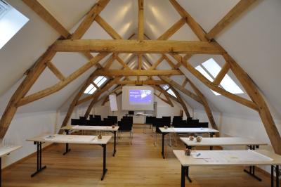 Salle de réunion lumineuse sous combles avec poutres apparentes, tables, chaises et écran de projection installé.