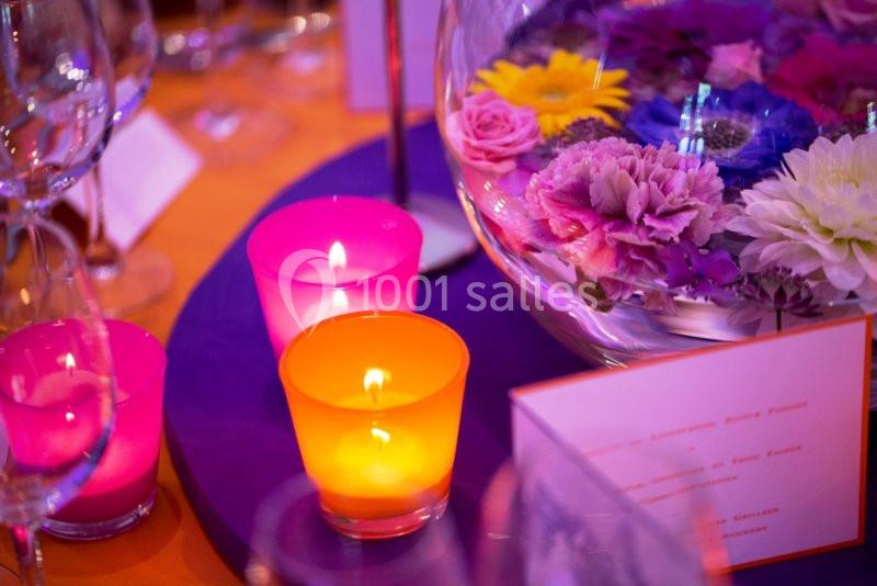 Bougies colorées allumées et fleurs flottantes dans un vase en verre sur une table décorée.