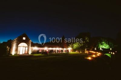 Vue d'un bâtiment en briques avec une tour, entouré d'arbres, d'une pelouse et d'un étang.
