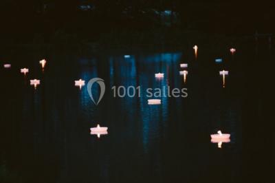 Vue d'un bâtiment en briques avec une tour, entouré d'arbres, d'une pelouse et d'un étang.