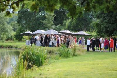 Vue d'un bâtiment en briques avec une tour, entouré d'arbres, d'une pelouse et d'un étang.