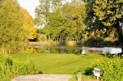 Vue d'un bâtiment en briques avec une tour, entouré d'arbres, d'une pelouse et d'un étang.