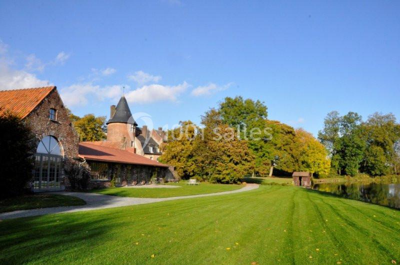 Bâtiments en briques avec une tour, entourés d'un parc verdoyant et d'un plan d'eau sous un ciel dégagé.