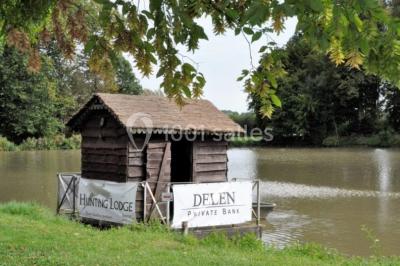 Vue d'un bâtiment en briques avec une tour, entouré d'arbres, d'une pelouse et d'un étang.