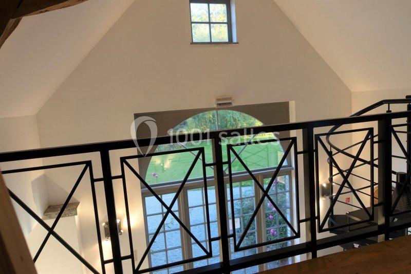 Vue depuis une mezzanine sur une grande baie vitrée donnant sur un jardin, avec une rambarde en métal au premier plan.