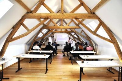Vue d'un bâtiment en briques avec une tour, entouré d'arbres, d'une pelouse et d'un étang.