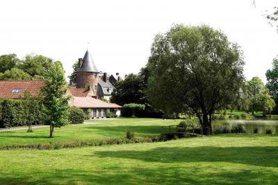 Vue d'un bâtiment en briques avec une tour, entouré d'arbres, d'une pelouse et d'un étang.
