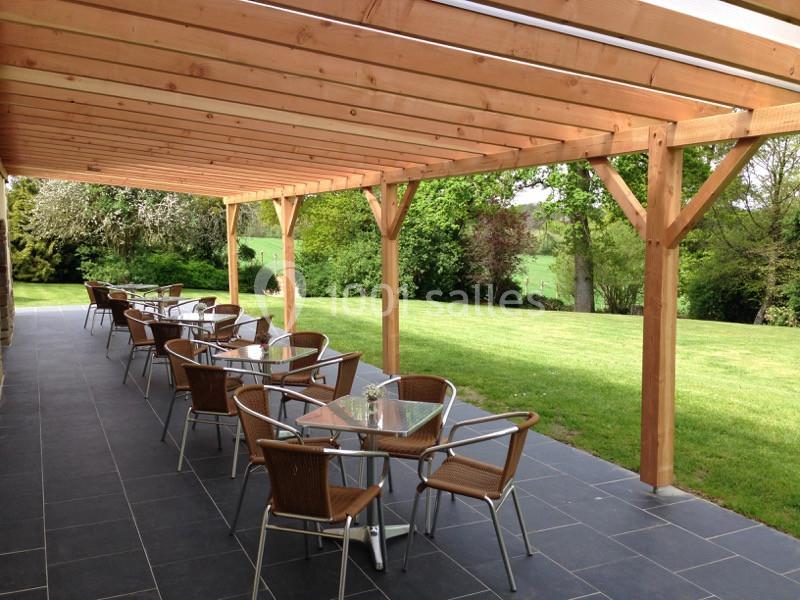 Terrasse couverte en bois avec tables et chaises en métal, donnant sur un jardin verdoyant.