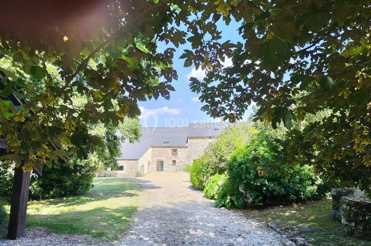 Allée gravillonnée bordée de végétation menant à une maison en pierre sous un ciel bleu dégagé.