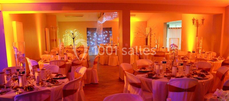 Salle de réception décorée avec des tables rondes, nappes blanches et éclairage chaleureux aux tons orange et jaune.