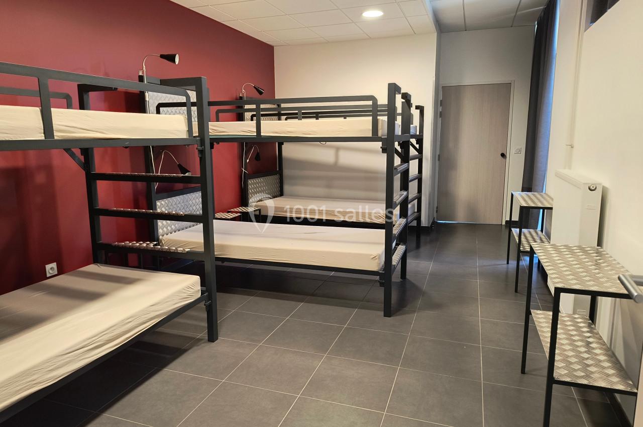 Dortoir avec lits superposés en métal, murs rouges et blancs, tables en métal et sol en carrelage gris.