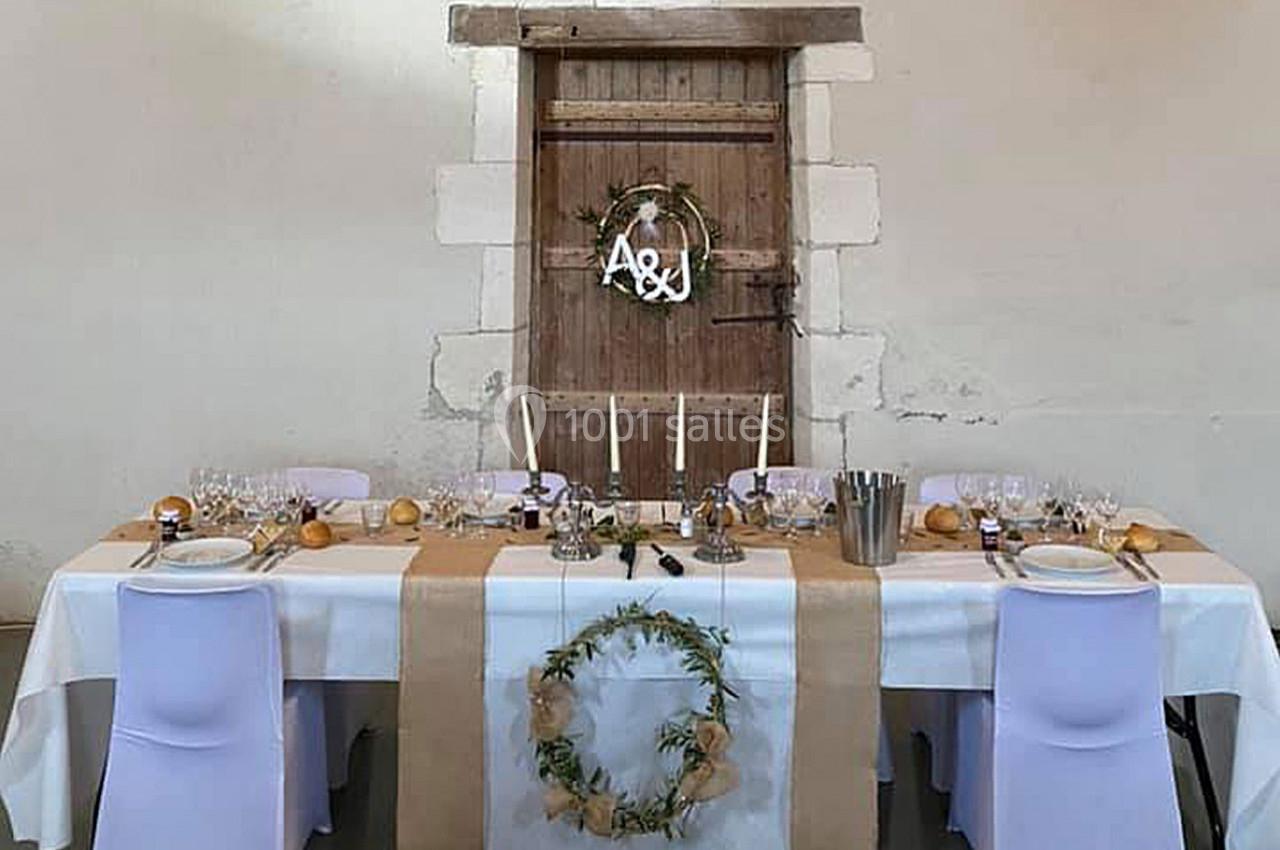 Table décorée pour un repas, ornée de nappes blanches et beige, avec bougies et couronnes végétales devant une porte en bois.