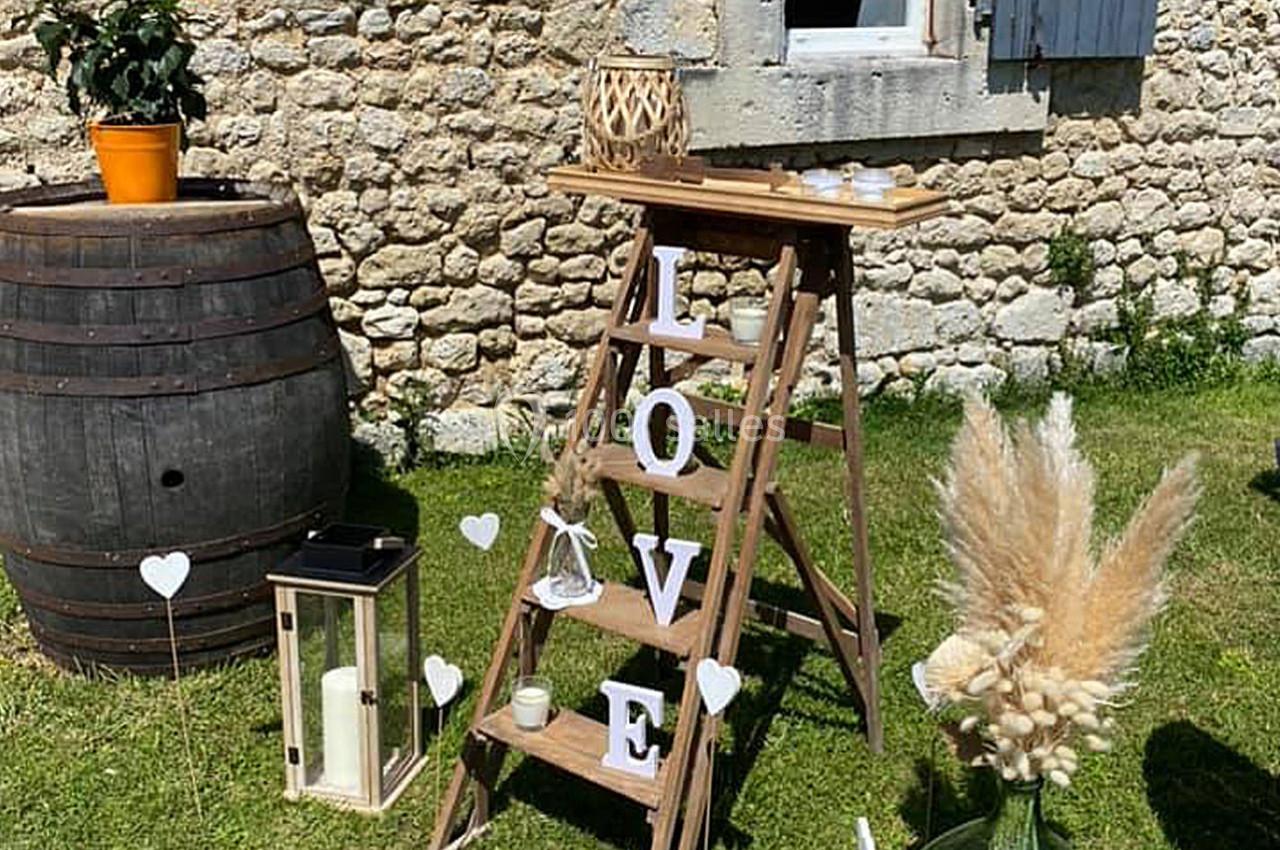 Échelle en bois décorée avec des lettres formant ’LOVE’, entourée de bougies, fleurs séchées et lanternes dans un jardin.