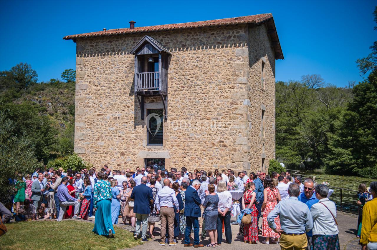 Groupe de personnes rassemblées devant un bâtiment en pierre sous un ciel bleu, entouré de verdure.
