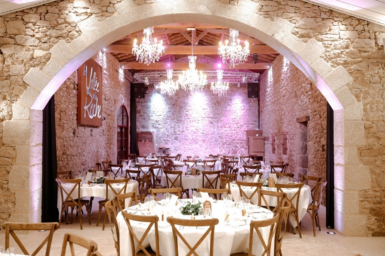 Salle de réception en pierre avec tables dressées, chaises en bois et lustres suspendus.