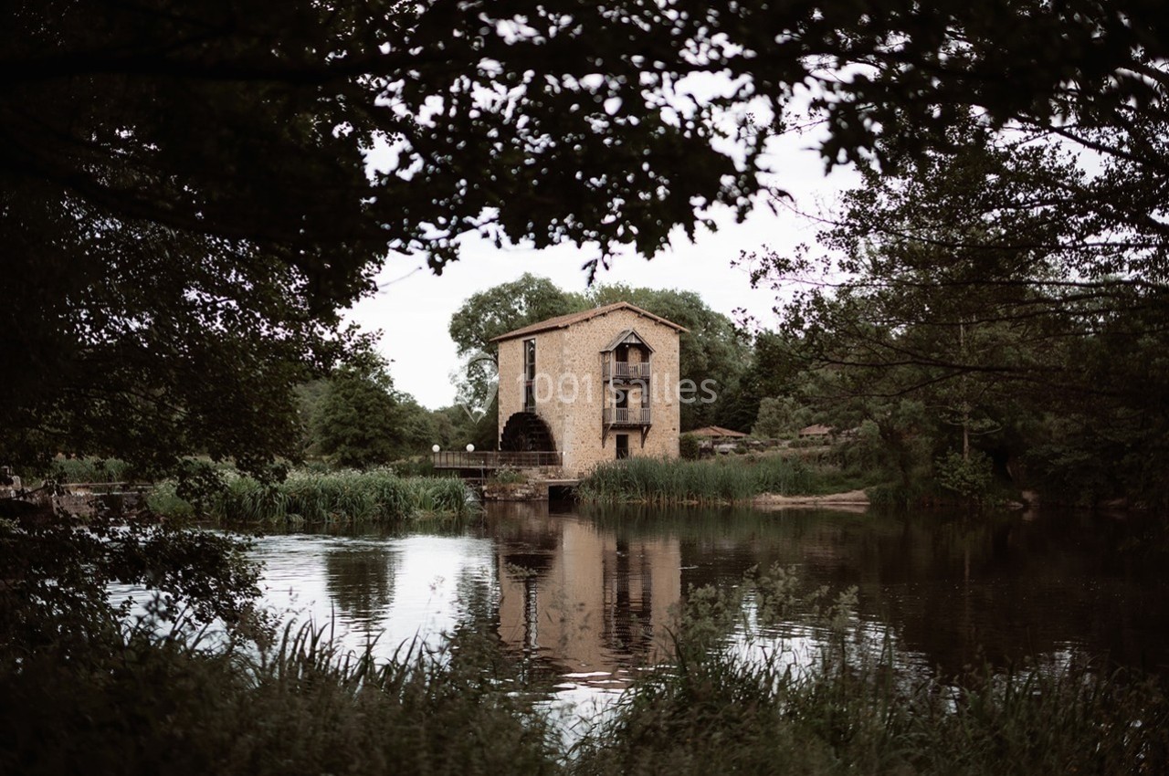 Vue d'un ancien moulin en pierre au bord d'une rivière, entouré de végétation et d'arbres.