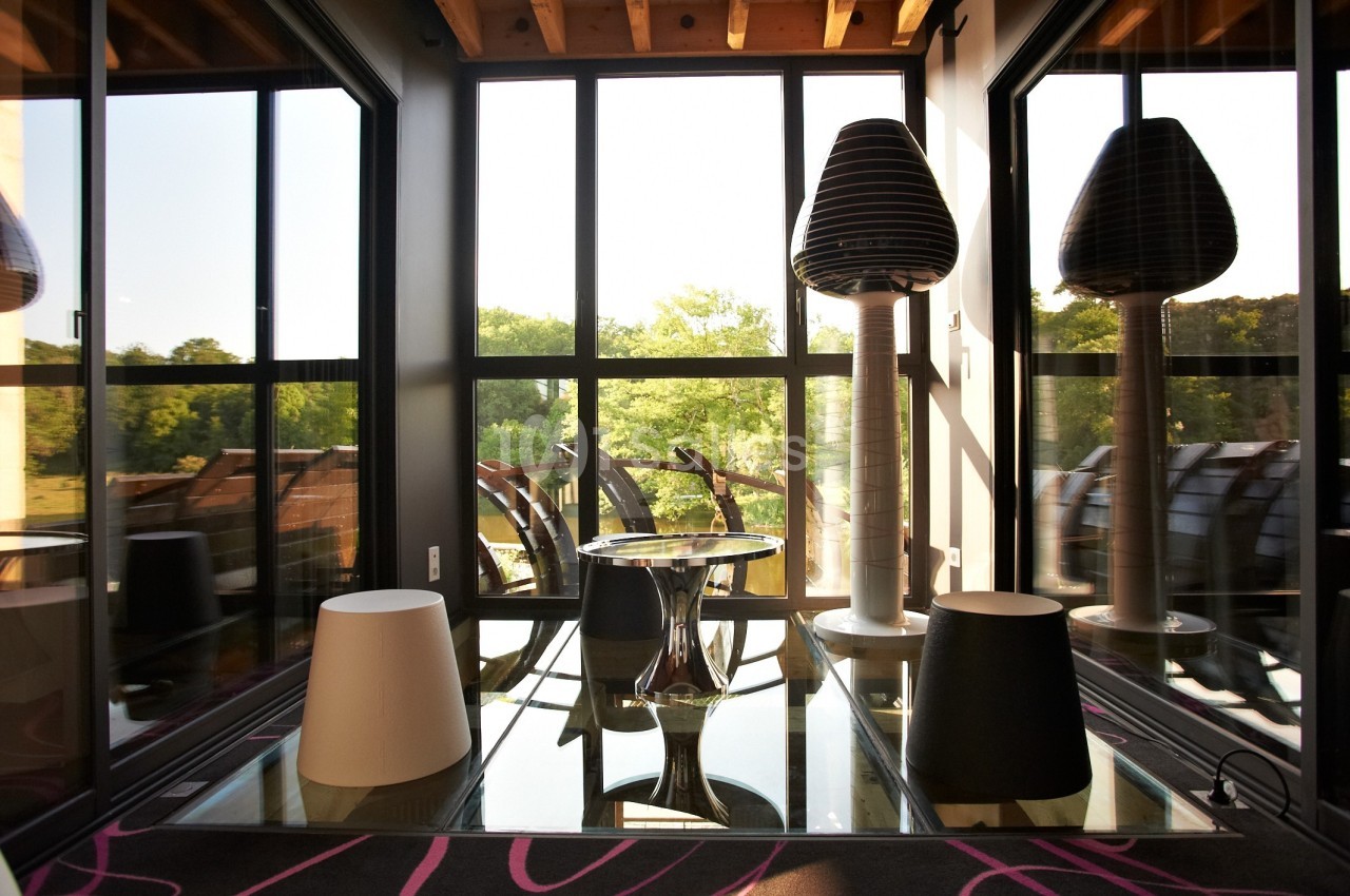 Salle lumineuse avec grandes baies vitrées, mobilier moderne et vue sur un paysage verdoyant à l'extérieur.