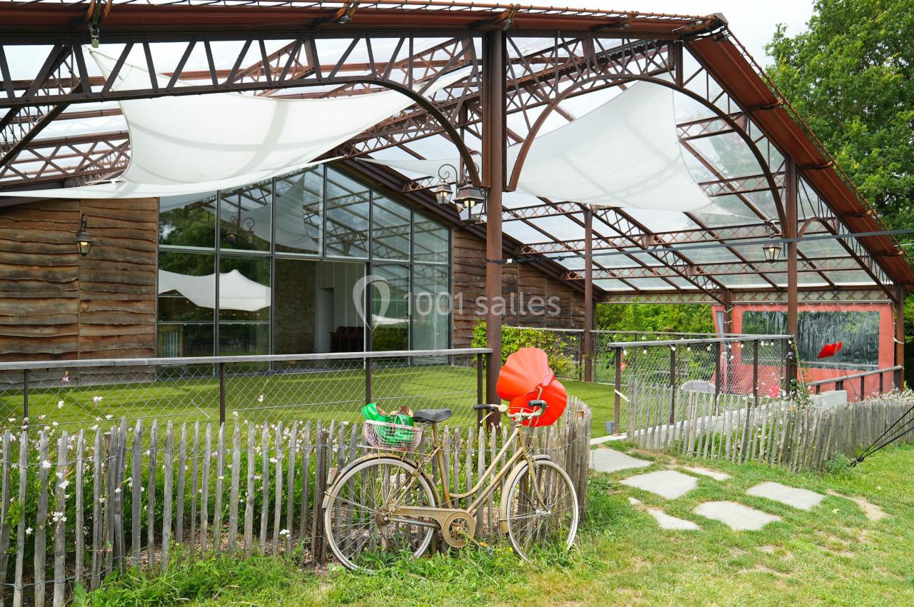 Un vélo ancien est appuyé contre une clôture devant une structure en bois et verre avec des voiles tendues.