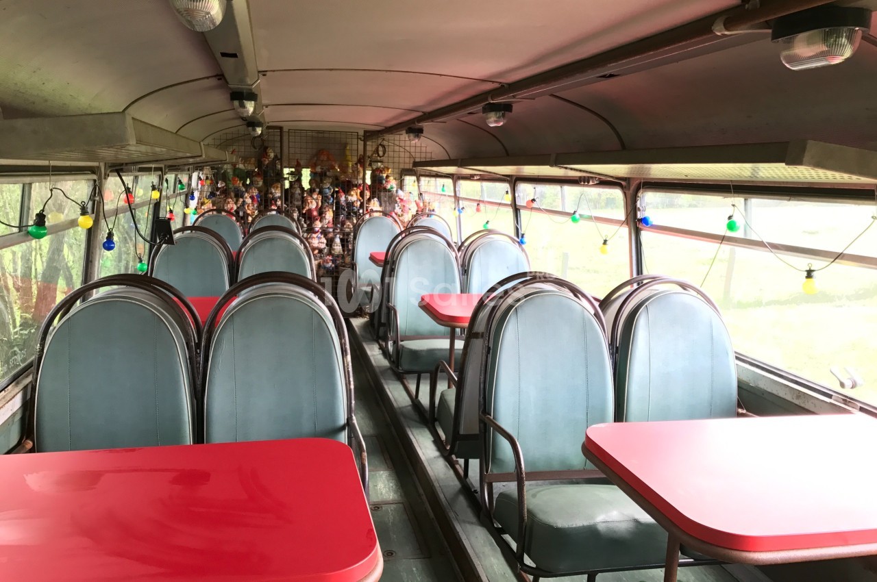 Intérieur d'un ancien bus aménagé en espace de restauration avec des tables rouges et des chaises bleues.
