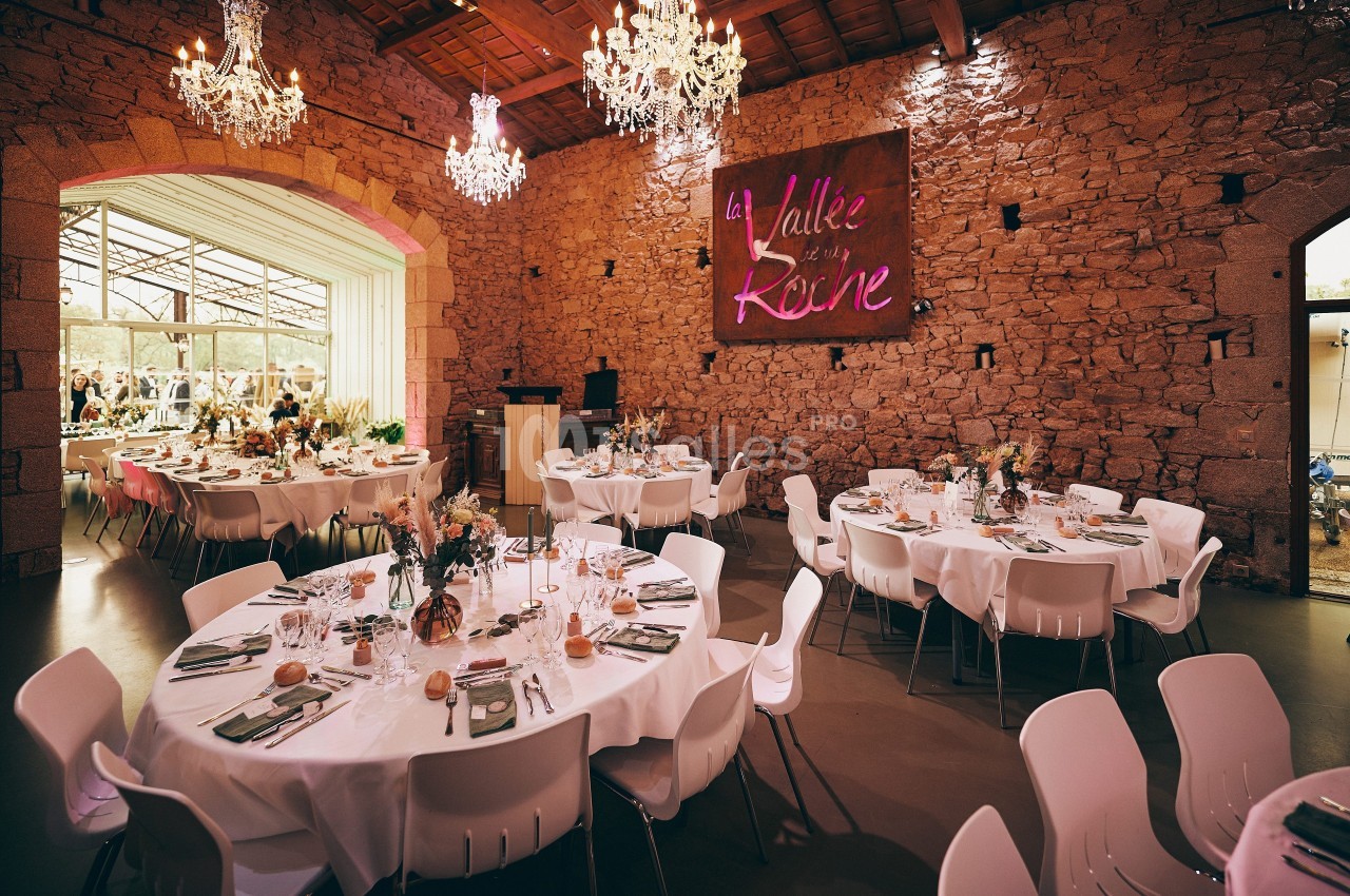 Salle de réception avec murs en pierre, tables rondes dressées et lustres suspendus.