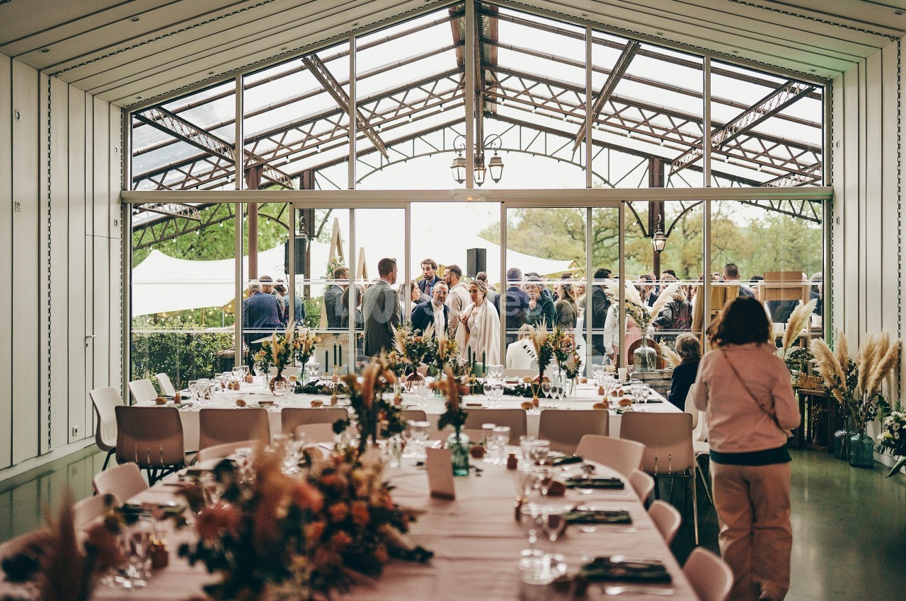 Salle de réception décorée avec des tables dressées, donnant sur une terrasse où des invités sont rassemblés.