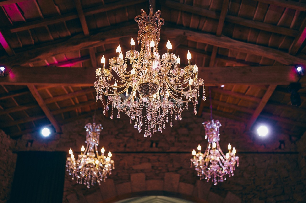 Trois lustres en cristal éclairés suspendus sous un plafond en bois dans une salle en pierre.