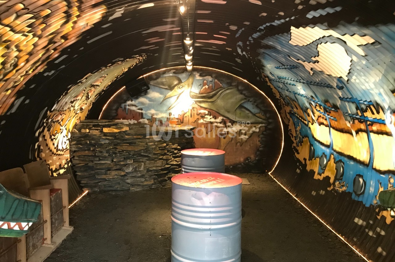 Intérieur d'un tunnel décoré de peintures murales colorées avec des barils métalliques au centre.