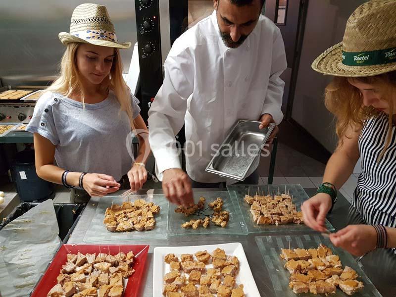 Un chef et deux personnes préparent et disposent des morceaux de nougat sur des plateaux dans une cuisine.
