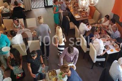 Des personnes se servent à un buffet varié disposé sur des tables rondes dans une salle lumineuse.