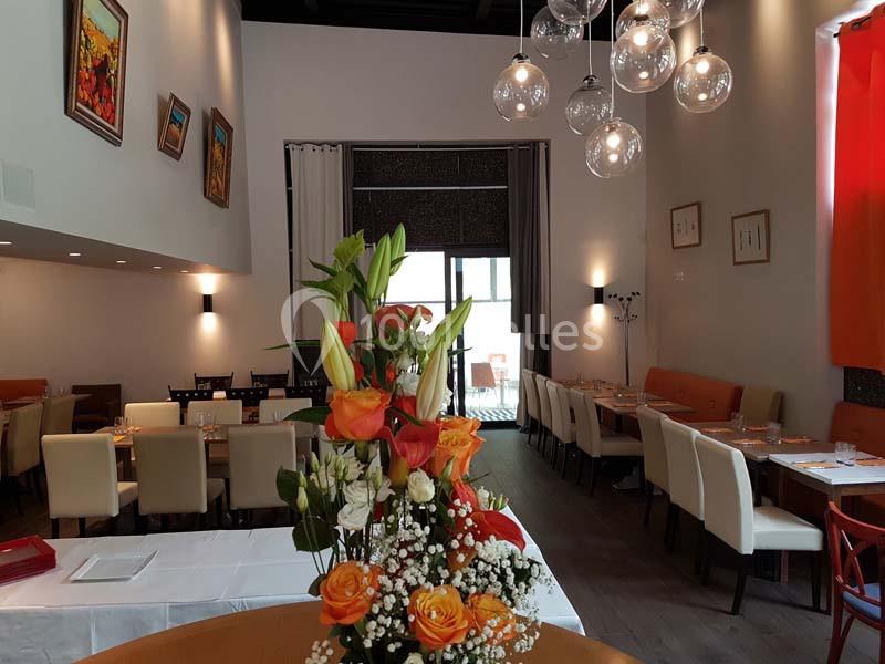 Salle de restaurant élégante avec tables dressées, décor moderne et bouquet de fleurs au premier plan.