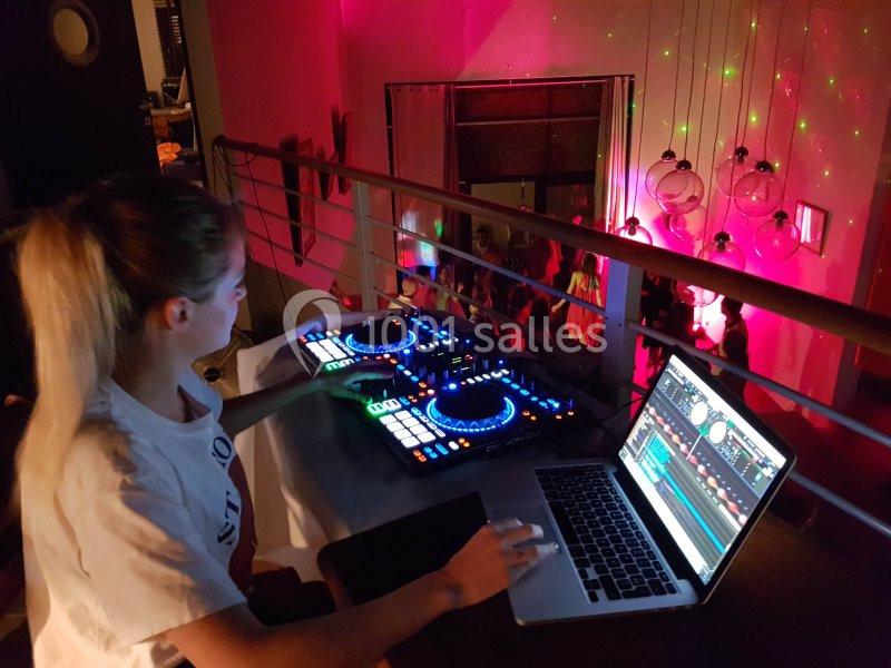 Une DJ utilise une console de mixage et un ordinateur portable dans une salle éclairée par des lumières colorées.