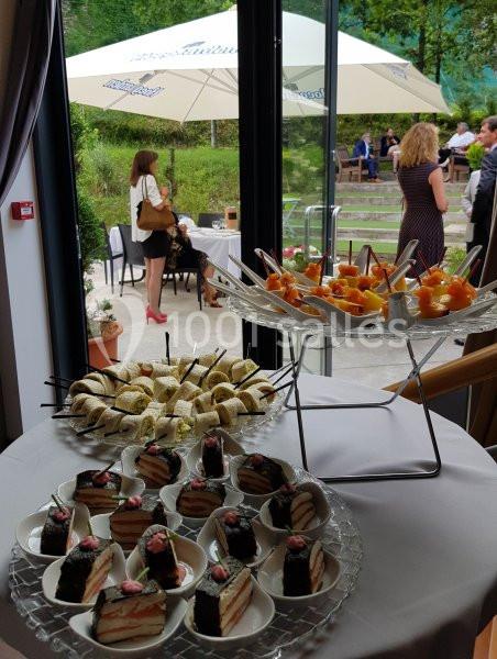 Buffet avec desserts variés, verrines et gâteaux, disposé près d'une baie vitrée donnant sur une terrasse animée.