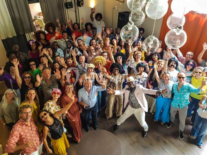 Groupe de personnes en tenue colorée dans une salle, souriant et levant les bras lors d'un événement festif.