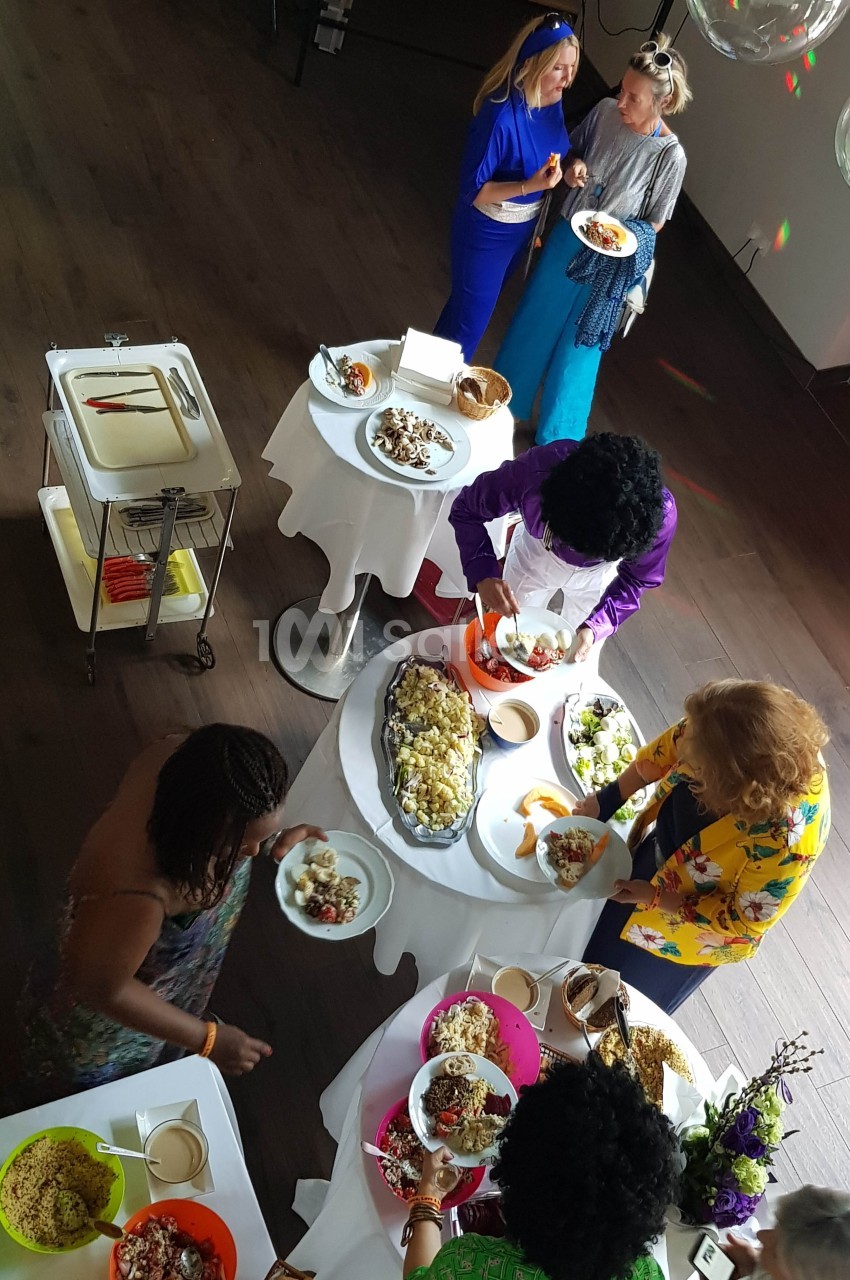 Des personnes se servent à un buffet varié disposé sur des tables rondes dans une salle au sol sombre.