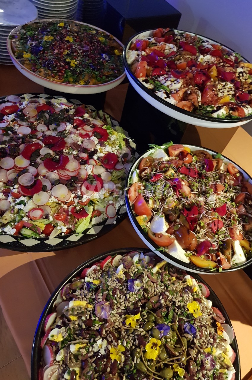 Assortiment de salades colorées garnies de légumes frais, graines, fleurs comestibles et herbes, présentées sur une table.