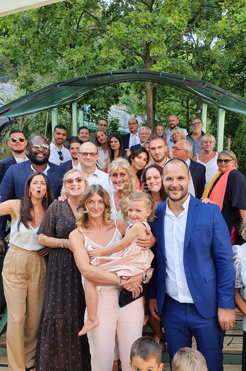 Groupe de personnes posant ensemble en extérieur sous une arche, entourées de verdure.