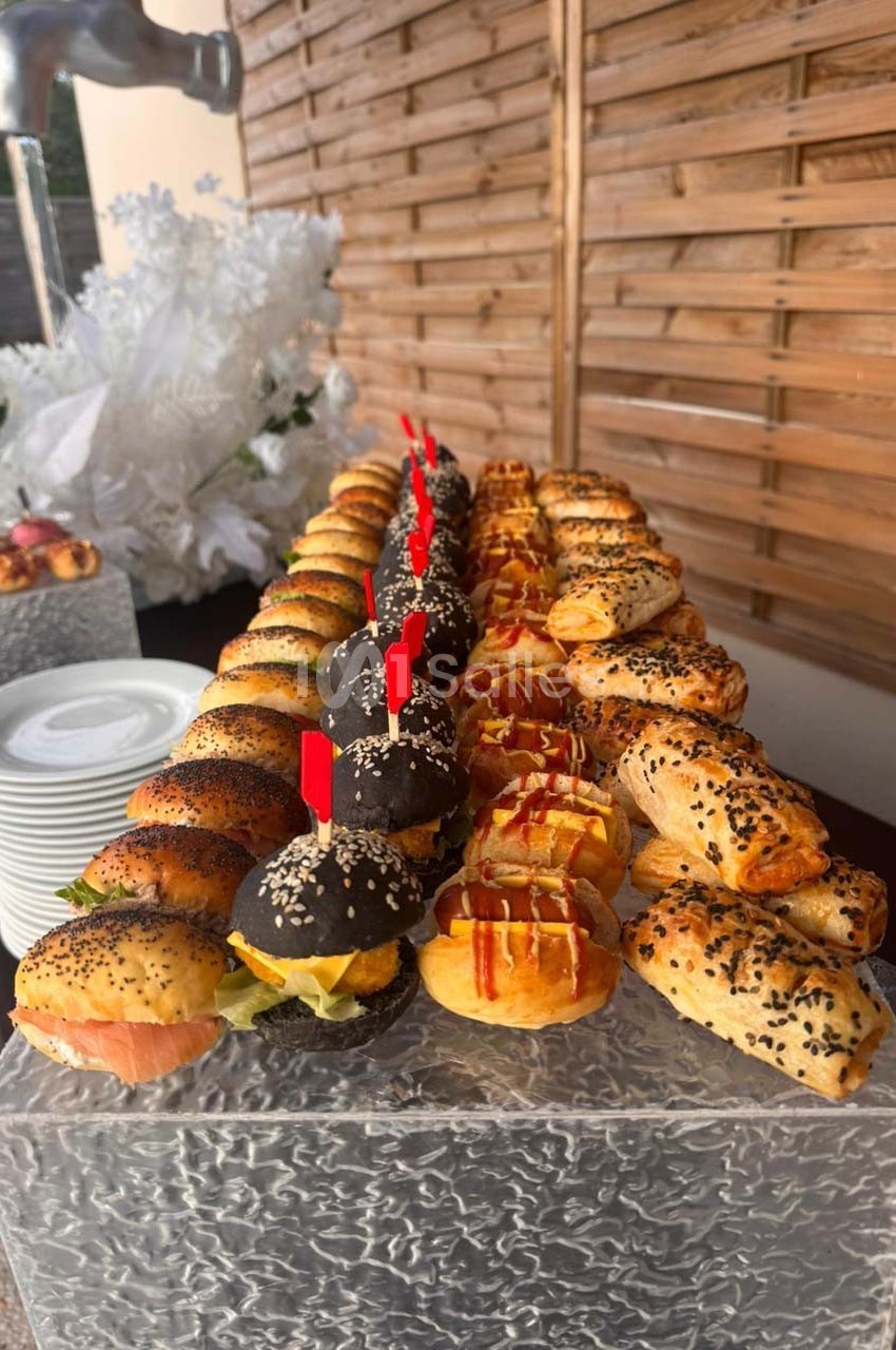 Plateau de mini-sandwichs variés et feuilletés garnis, disposés sur une table en extérieur avec une décoration blanche.
