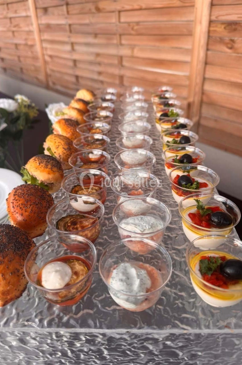 Plateau de verrines et mini-burgers disposés en rangées sur une table avec un fond en bois.