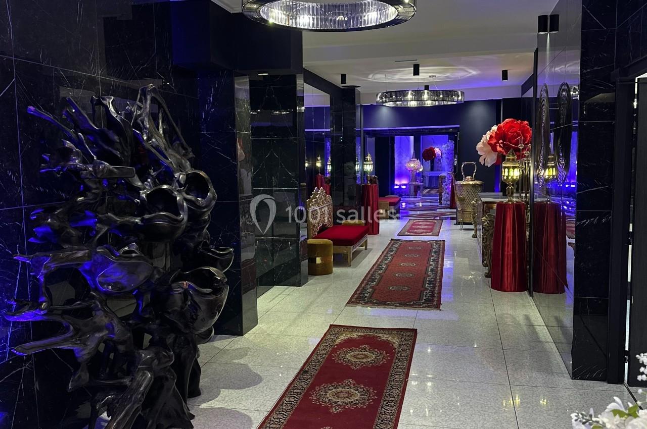 Couloir élégant avec tapis rouges, murs noirs brillants, éclairage bleu et décoration moderne, dont un lustre central.