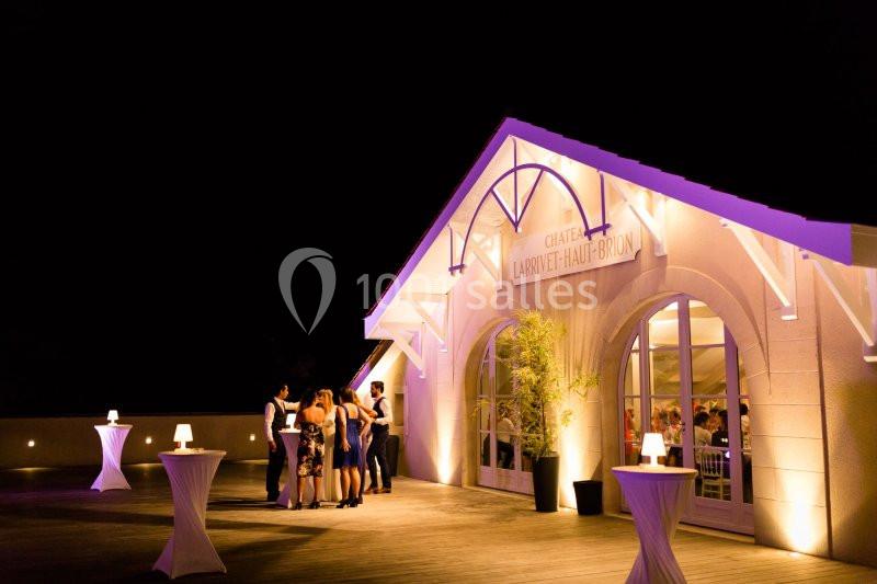 Groupe de personnes discutant sur une terrasse éclairée devant un bâtiment blanc, de nuit.